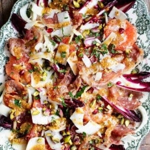 A close up of a festive salad on a serving plate made with blood orange, chicory, fennel, prosciutto, pecorino, pomegranate and pistachios.