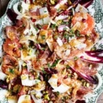 A green platter on a rustic wooden background with a big festive salad made with red endive, fennel, blood orange, prosciutto and pecorino.
