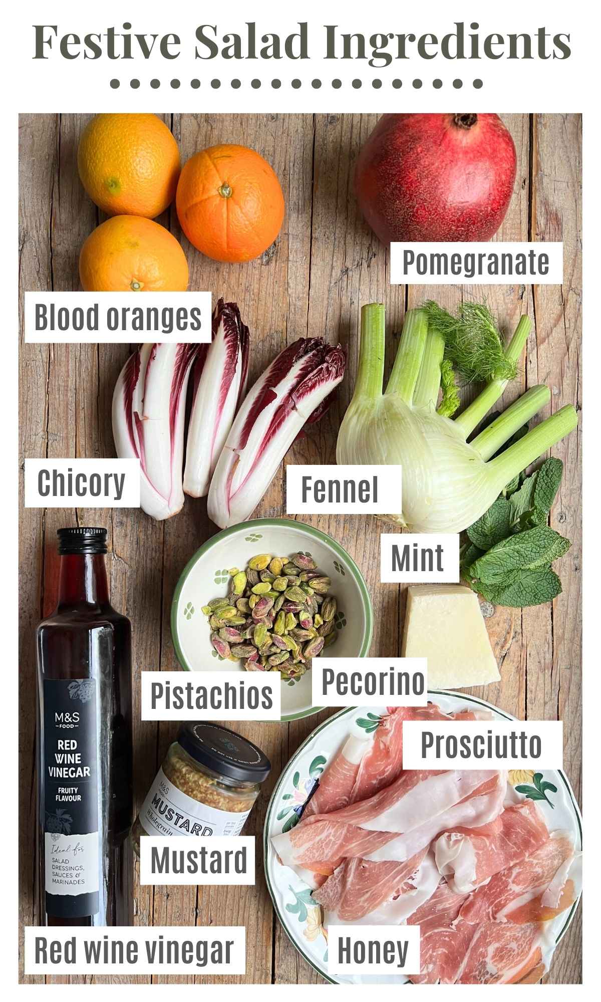 All the ingredients for a festive salad laying on a rustic wooden surface. The labels read: blood oranges, pomegranate, fennel, chicory, red wine vinegar, mustard, mint, honey, prosciutto, pistachios and pecorino.