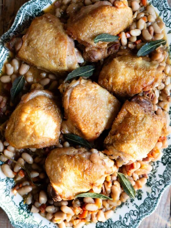 Italian braised chicken thighs on a bed of cannellini beans and vegetables served on a green vintage style serving plate.
