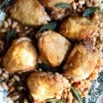 An overhead shot of braised chicken thighs on a bed of cannellini beans and vegetables. The serving plate is green vintage style.