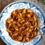 Past and lentils in a blue and white bowl sitting on a rustic wooden surface with sprigs of rosemary around and a glass of white wine.