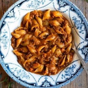 Pasta and lentils in a blue and white vintage bowl sitting on a wooden surface.