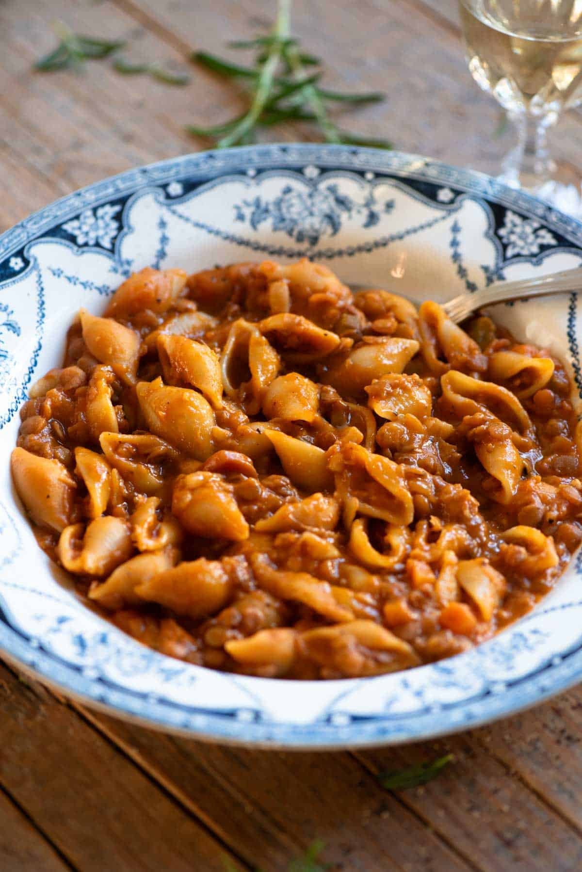 A close up of pasta and lentils in a blue vintage style bowl with a spoon.