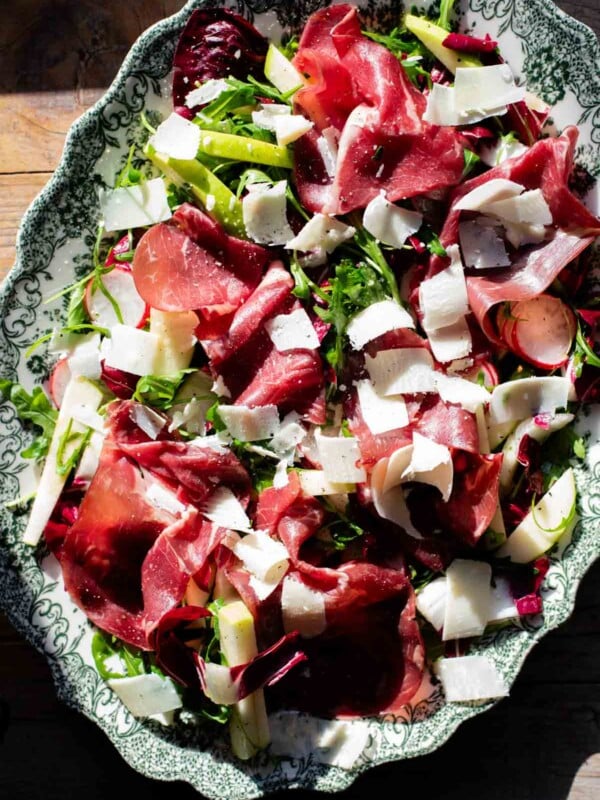 A salad with Bresaola, radicchio, radish and apple in direct sunlight on a large green and white platter.