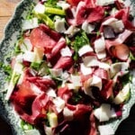 A close up of a bresaola salad topped with shavings of Parmigiano Reggiano on a servings plate.