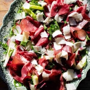 A close up of a bresaola salad topped with shavings of Parmigiano Reggiano on a servings plate.