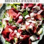 An overhead shot of a bresaola salad with shavings of Parmigiano Reggiano cheese. The text overlay reads: Italian Salad Bresaola and Radicchio.