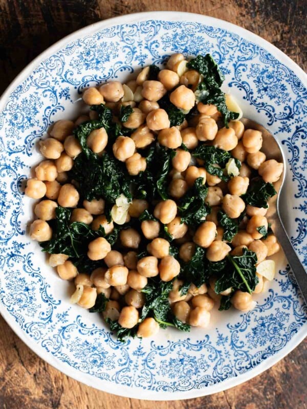 Chickpeas with garlic and cavolo nero in a blue and white bowl sitting on a rustic wooden surface.