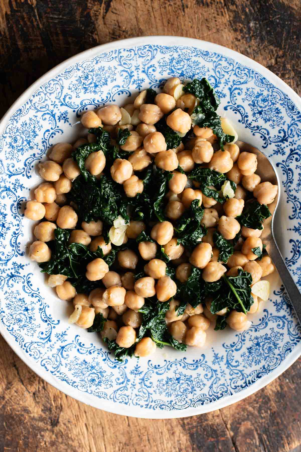 Chickpeas with garlic and cavolo nero in a blue and white bowl sitting on a rustic wooden surface.