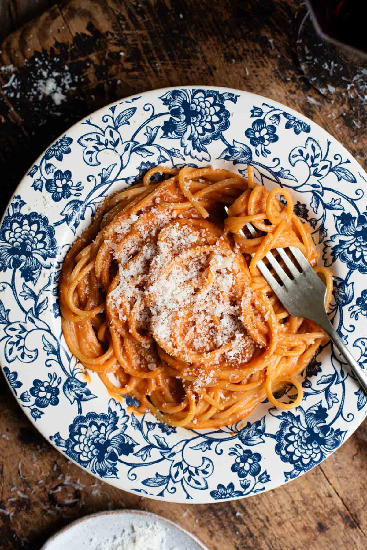Spaghetti with a creamy roasted red pepper sauce in a blue floral bowl sitting on a wooden board.