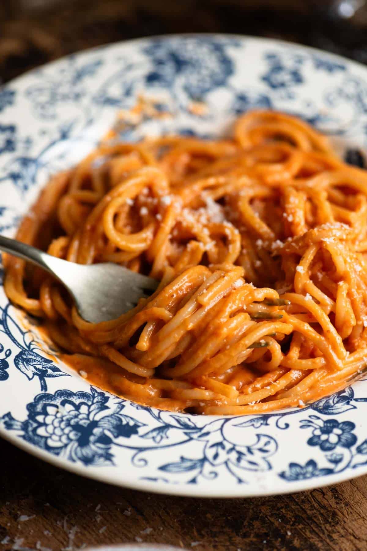 A close up of spaghetti with creamy roasted red pepper sauce rolled around a fork.