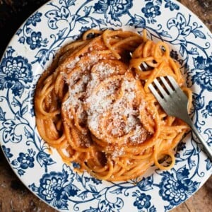 A close up of creamy roasted red pasta in a blue floral bowl sitting on a wooden board.