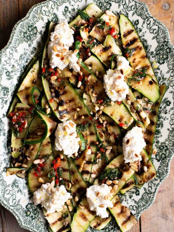 An overhead shot of grilled zucchini on a serving platter topped with garlic, chilli, mint and ricotta.
