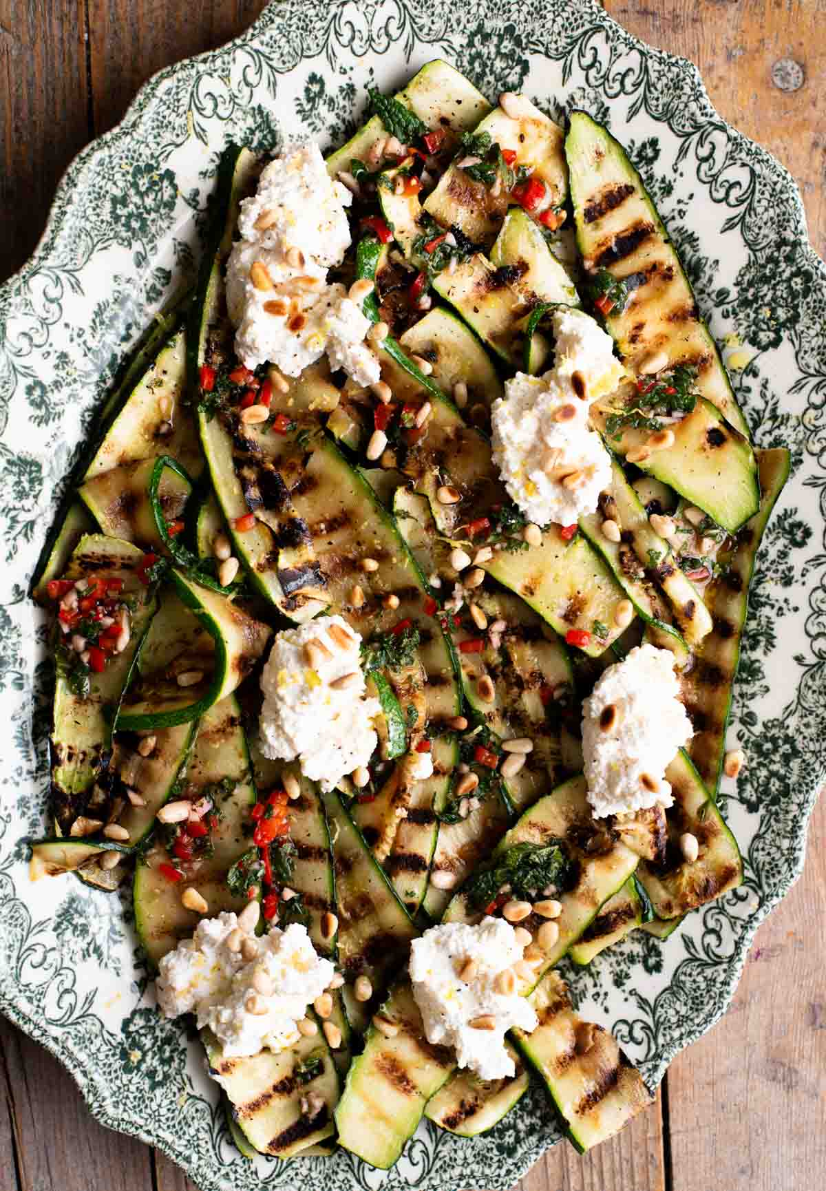 An overhead shot of grilled zucchini on a serving platter topped with garlic, chilli, mint and ricotta.