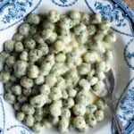 Overhead view of mini spinach gnocchi in a creamy butter and cheese sauce served in a white bowl with a blue floral pattern and a spoon on the side.
