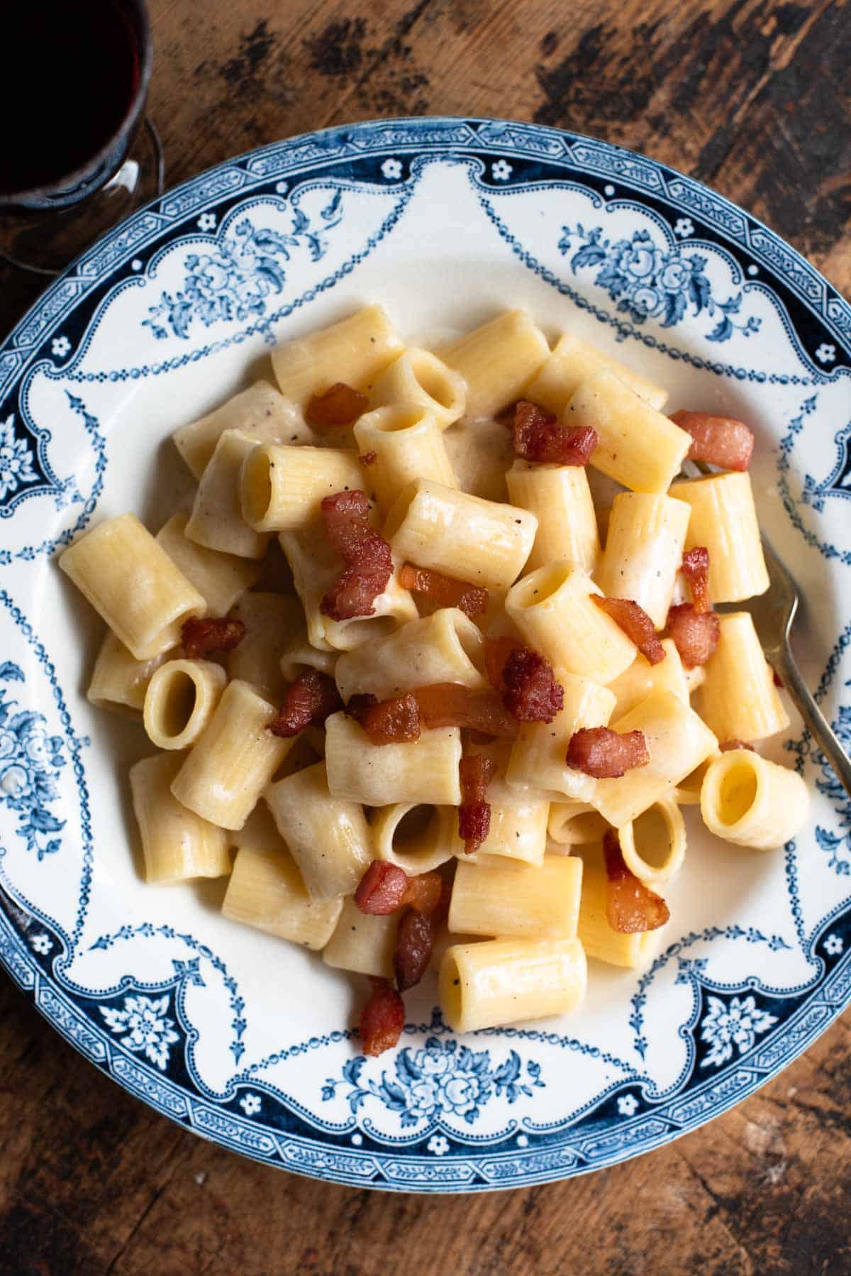 Pasta alla Gricia in a white and blue vintage style bowl sitting on a wooden surface.