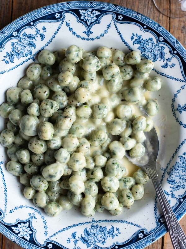 Mini spinach and potato gnocchi with a parmigiano and butter sauce in a blue and white bowl sitting on a wooden surface.