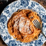 Spaghetti with a creamy roasted red pepper sauce in a blue and white floral bowl with a fork.