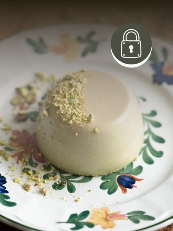 A pistachio panna cotta sitting on a floral plate on a wooden board.