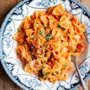 A close up of farfalle pasta in a garlic and chilli sauce with a fork at the side. The bowl is vintage style in blue and white.