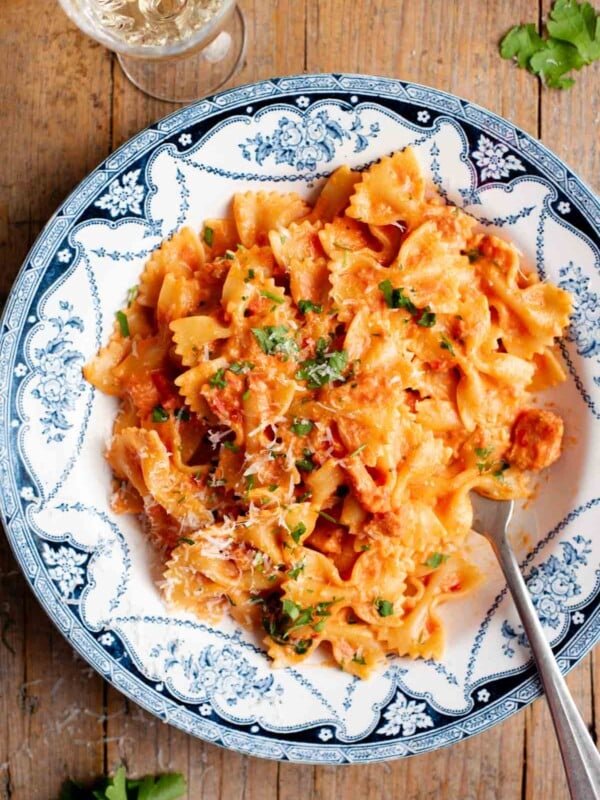 An overhead shot of farfalle pasta with a creamy tomato, garlic and chilli sauce in a blue and white bowl.