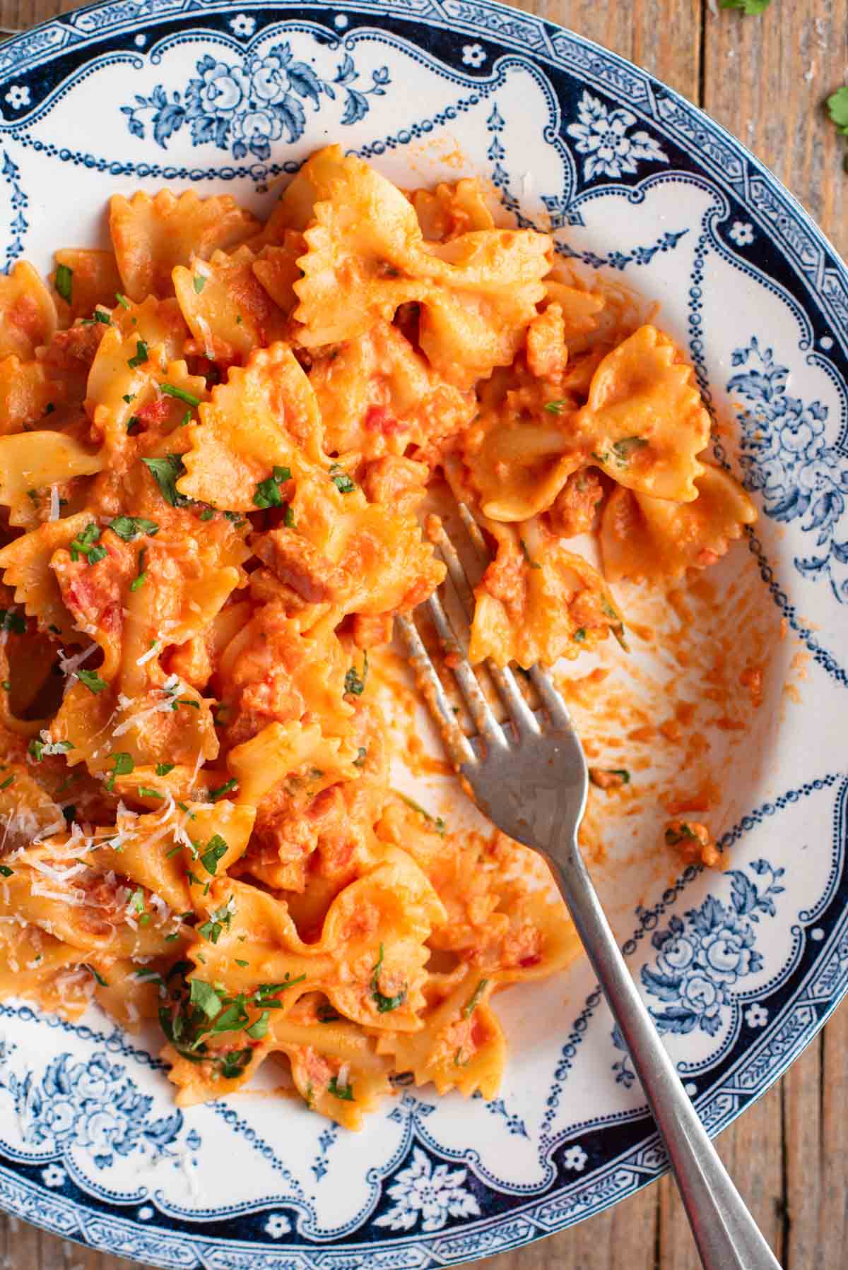A close up of farfalle pasta in a blue and white floral bowl with a fork.