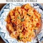 A pinterest graphic of a creamy tomato farfalle pasta with in a blue and white bowl. The text overlay reads: Farfalle Pasta with garlic and chilli.