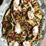 A close up of grilled zucchini on a serving plate topped with mint, chilli and fresh ricotta.