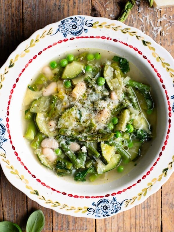 Spring soup, Minestrone Primavera with lots of green vegetables in a clear broth in a vintage patterned bowl on a wooden background.