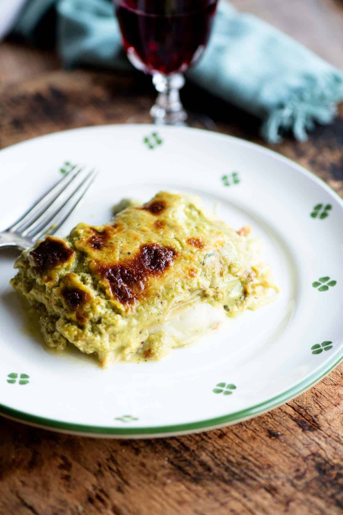 A slice of pistachio lasagna on a white plate with a fork at the side.