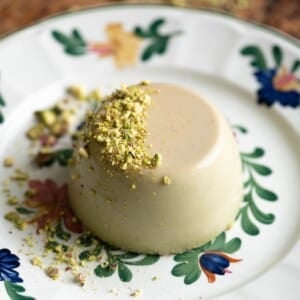 A close up of a pistachio panna cotta on a floral plate garnished with chopped pistachios.