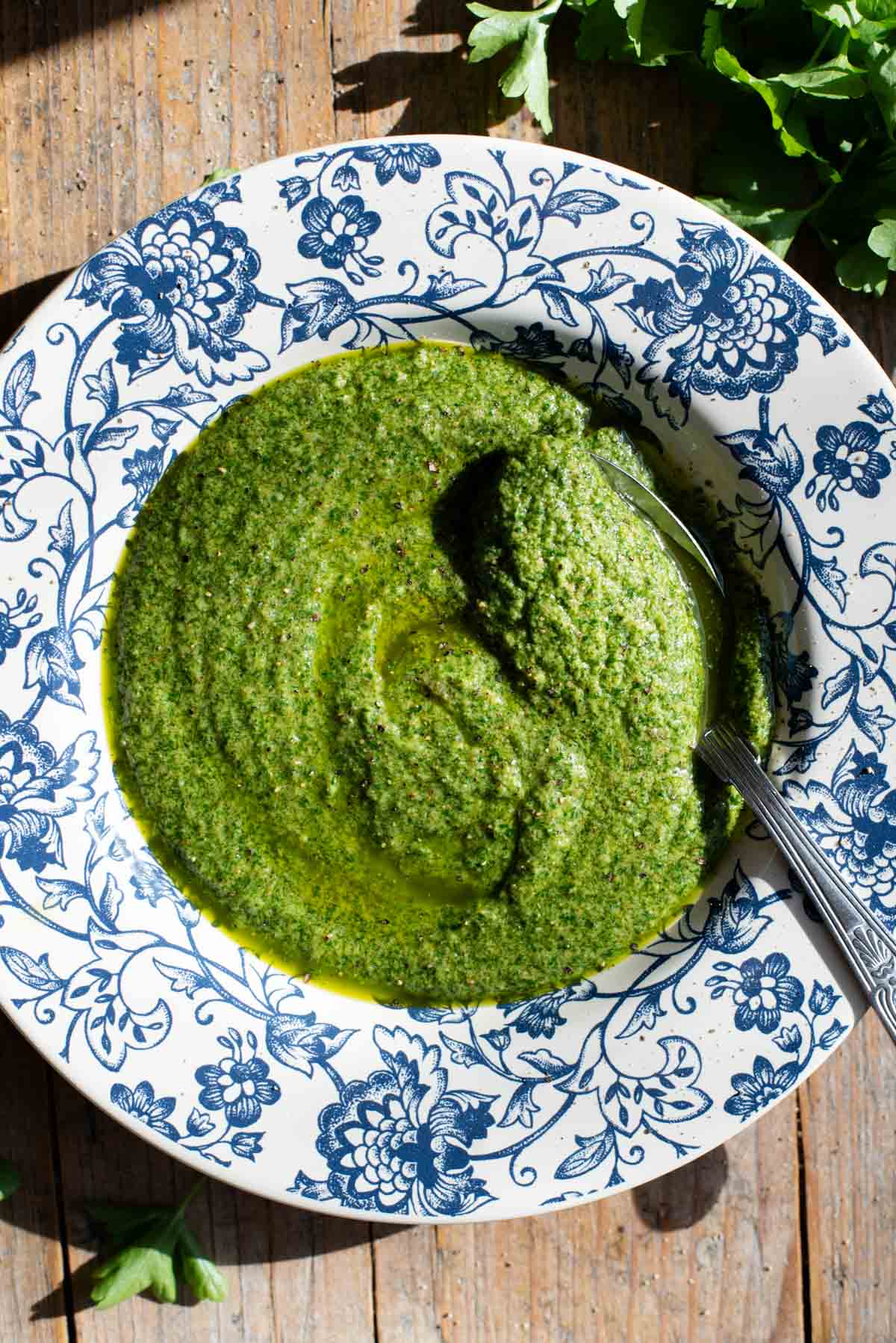 An overhead shot of a tuscan salsa verde in a blue and white bowl sitting on a wooden surface.
