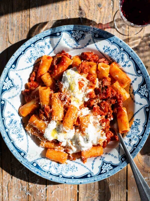 Spicy Calabrian sausage ragu with rigatoni pasta in a blue and white bowl topped with stracciatella cheese.