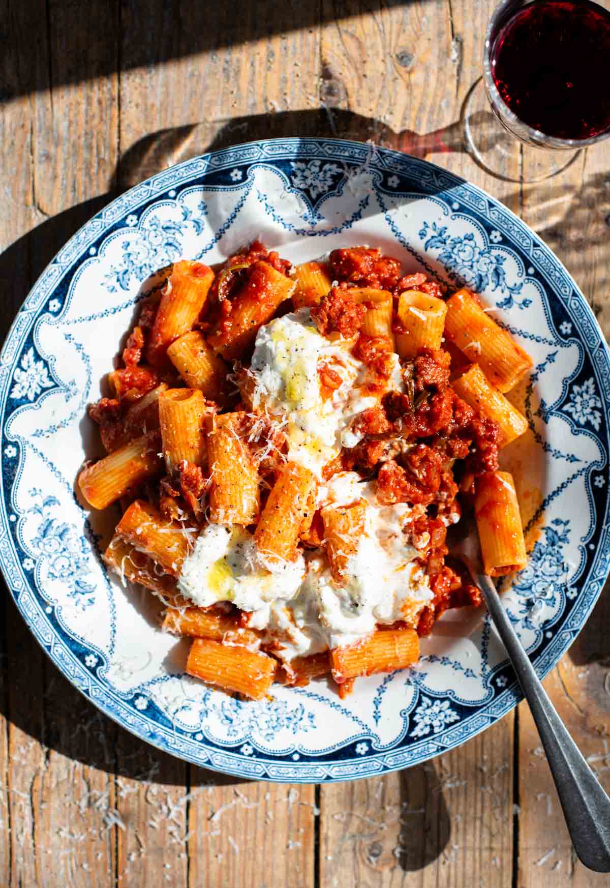 Spicy Calabrian sausage ragu with rigatoni pasta in a blue and white bowl topped with stracciatella cheese.