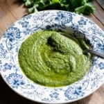 Salsa verde in a blue and white bowl with a spoon sitting on a rustic wooden background.