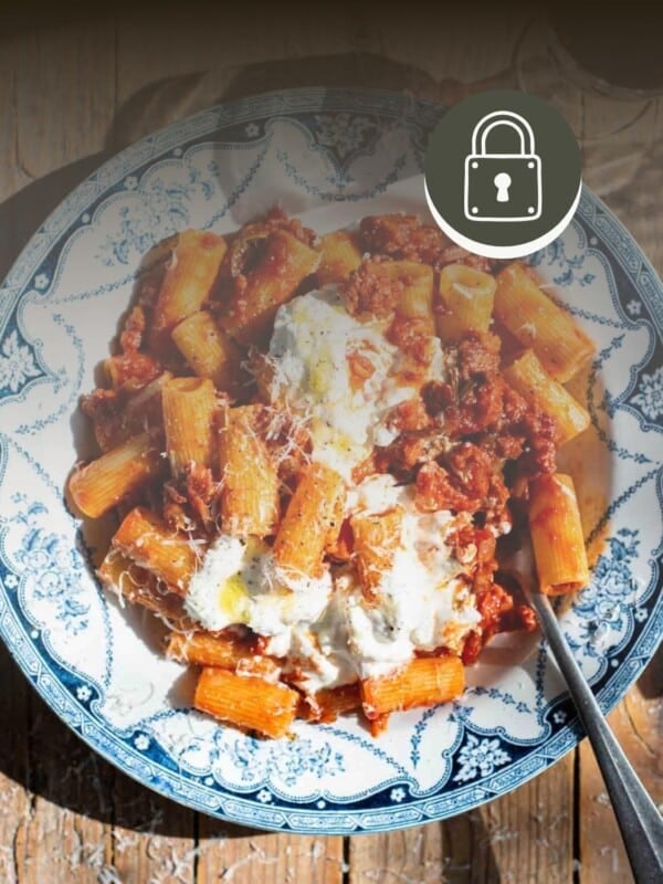 Spicy Calabrian sausage ragu in a blue and white bowl with stracciatella on top. The image is faded with a padlock symbol in the top right corner to signal a membership only recipe.