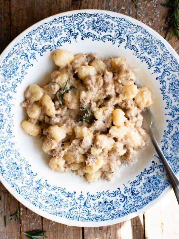 An overhead shot of gnocchi with a white creamy sausage ragu in a blue and white bowl on a rustic wooden surface.