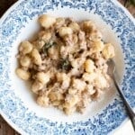 Gnocchi with a creamy white sausage and rosemary sauce in a blue and white bowl sitting on a wooden surface.