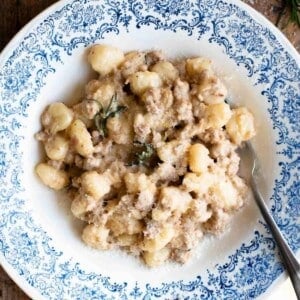 A close up of gnocchi with a creamy white sausage sauce with rosemary.