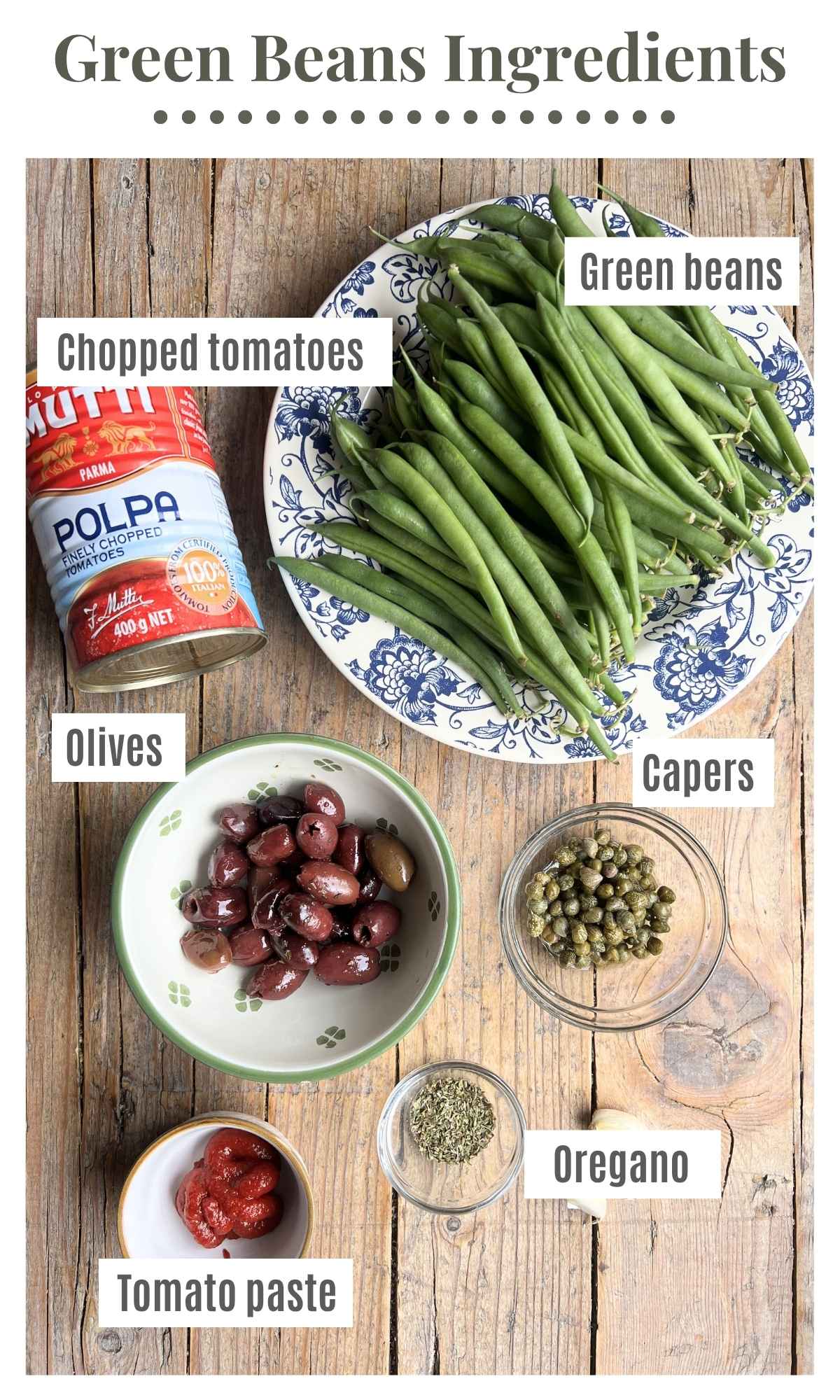 Canned tomatoes, green beans, olives, capers, oregano and tomato paste laying out on a rustic wooden board.
