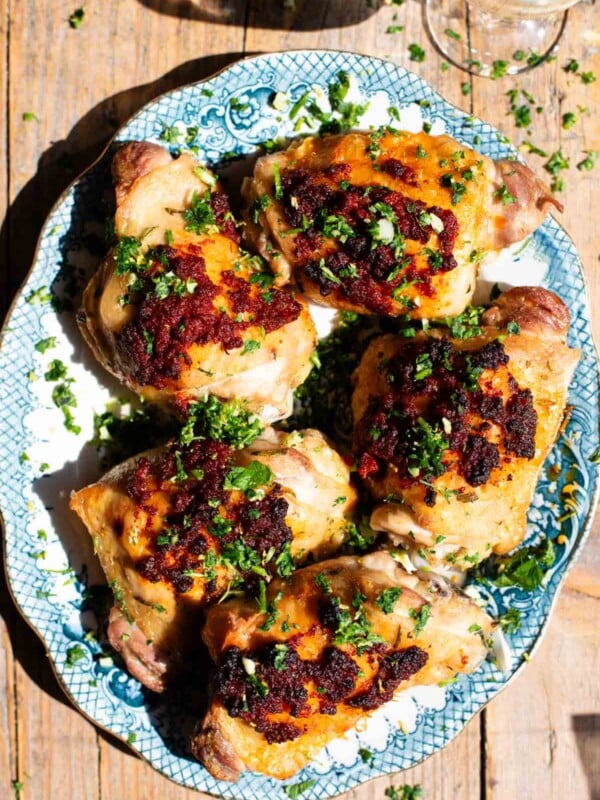 Baked chicken thighs with nduja on top sitting on a white and blue serving plate.