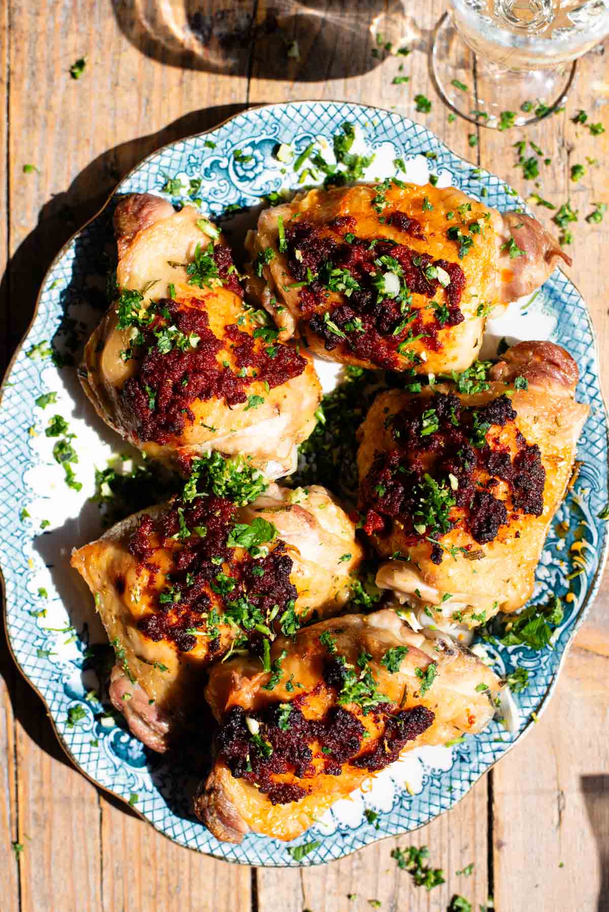 Baked chicken thighs with nduja on top sitting on a white and blue serving plate.