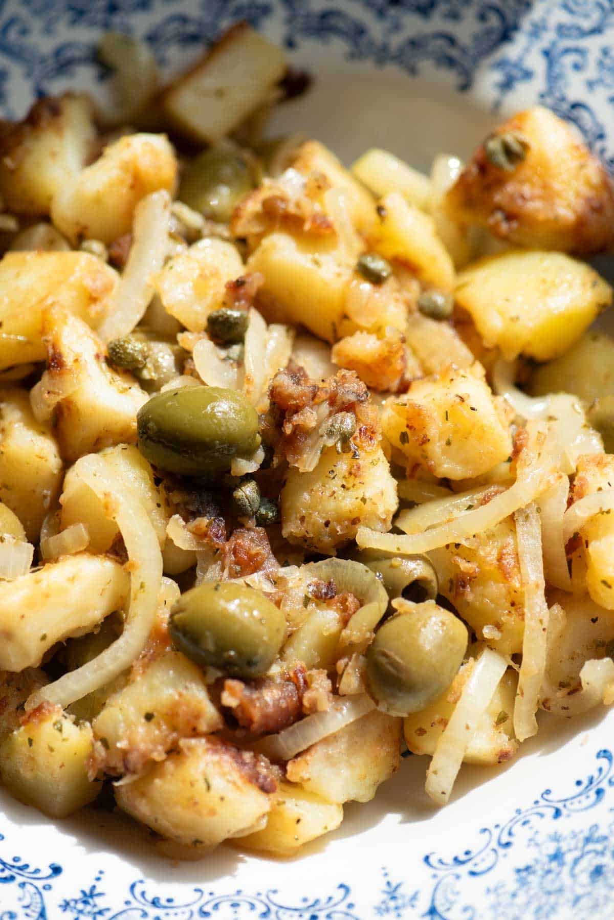 A close up of a potato side dish with olives, capers and oregano.