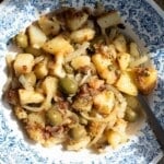 An overhead shot of a Sicilian potato dish with olives and capers in a blue bowl.
