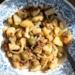 A close up of Sicilian potatoes in a blue bowl with capers and olives.