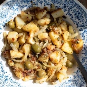 A close up of Sicilian potatoes in a blue bowl with capers and olives.