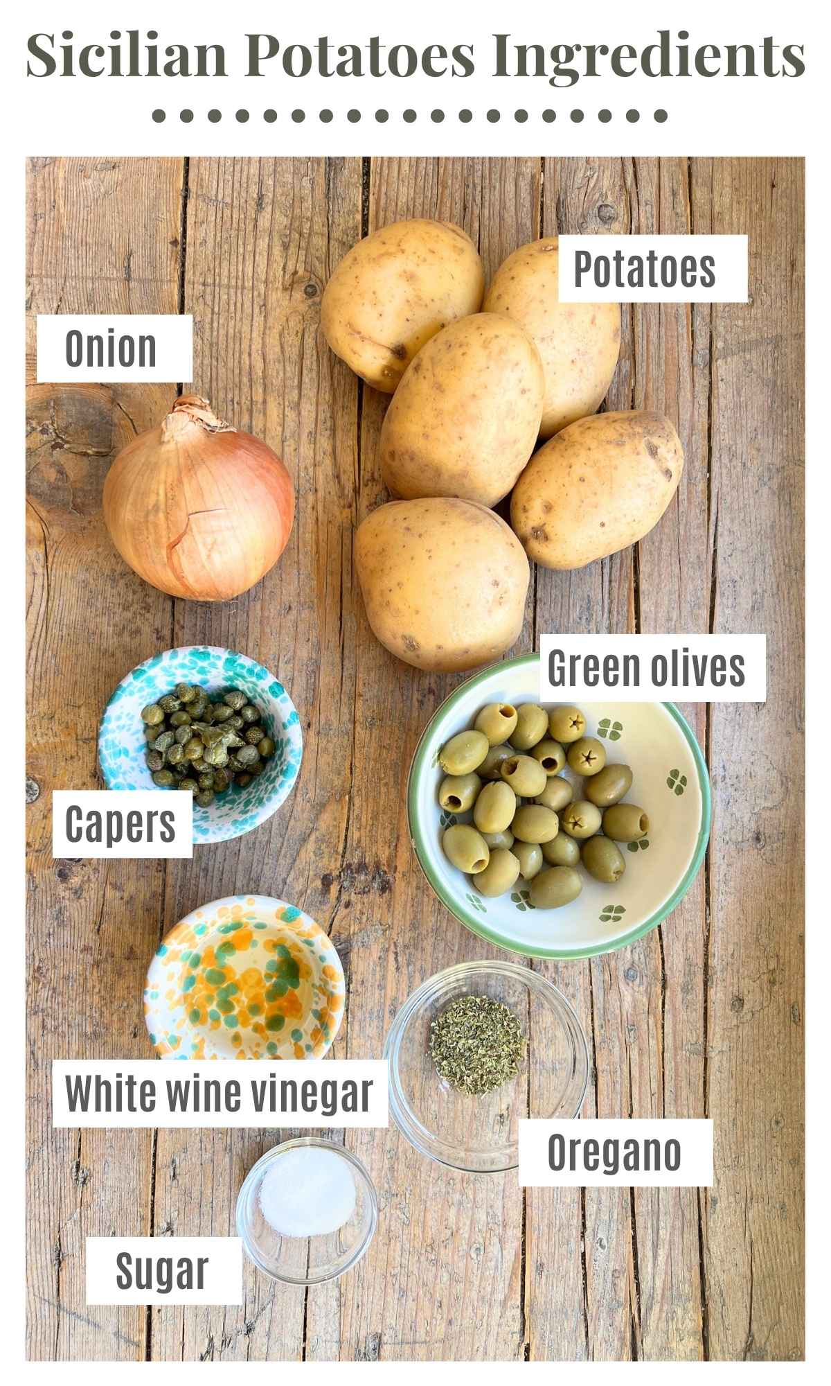 An overhead shot of all the ingredients needed to make a Sicilian potato side dish. Laid out are potatoes, onions, olives, capers, vinegar, sugar and oregano.