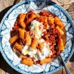 A close up of spicy calabrian sausage ragu in a blue and white bowl with stracciatella on top