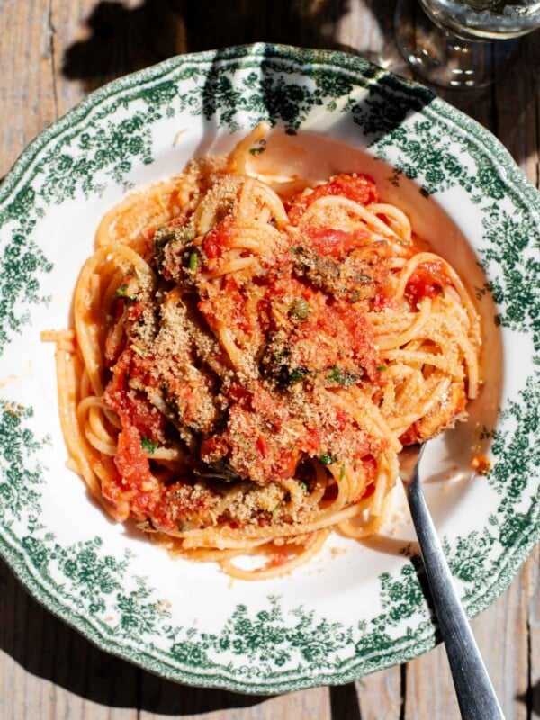 An overhead shot of spaghetti in a tomato sauce with sardines and breadcrumbs on top. The bowl is a vintage style green and white colour.